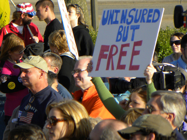 Photo of a tea party rally. A sign is visible that says, uninsured but free. 