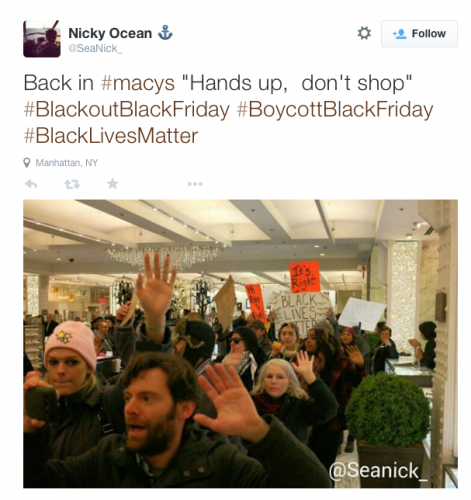 A tweeted picture of predominantly white faces with their hands up in a mall. Tweet reads: Back in #macys "hands up, don't shop" #blackoutblackFriday #boycottblackfriday #blacklivesmatter. tweet by @seanick_