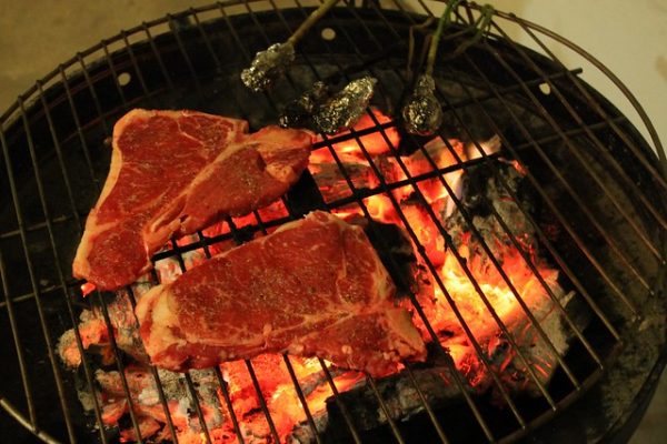 Photo of two steaks on a grill with an open flame. 