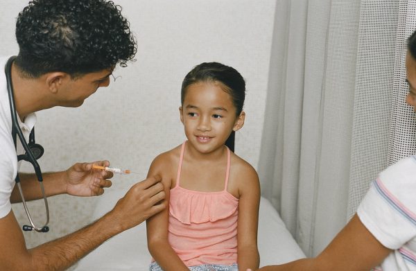 A young girl about to receive a vaccine. A parent holds her hand. 